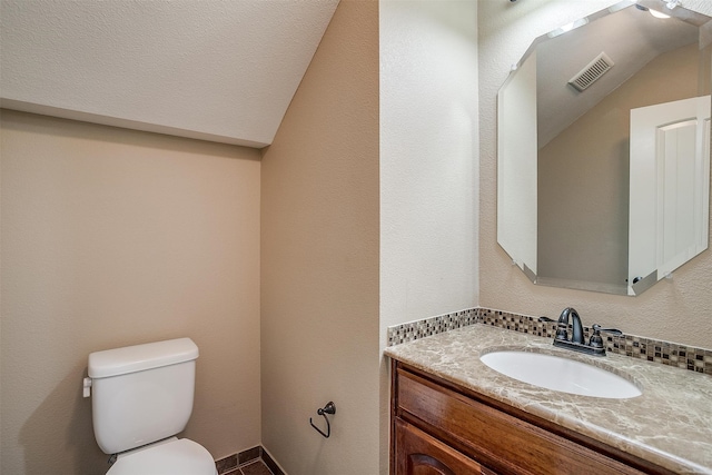 bathroom with lofted ceiling, a textured ceiling, vanity, and toilet