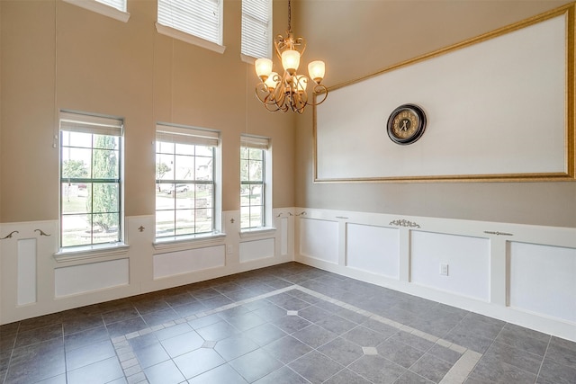 unfurnished dining area with a towering ceiling, a chandelier, and dark tile patterned floors