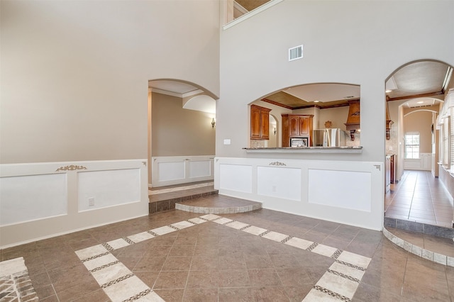 interior space with tile patterned flooring, ornamental molding, and a towering ceiling