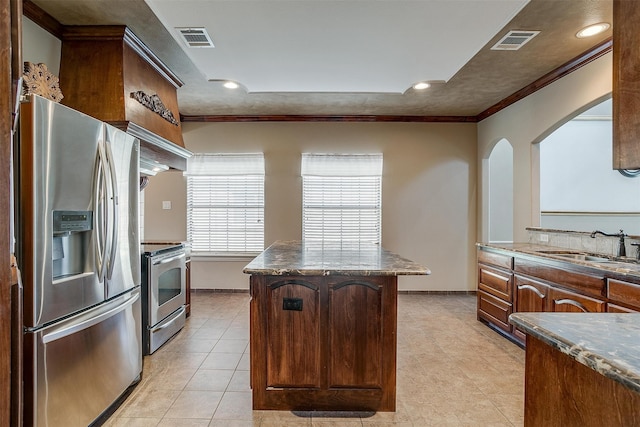 kitchen with sink, stainless steel appliances, a center island, dark stone counters, and crown molding