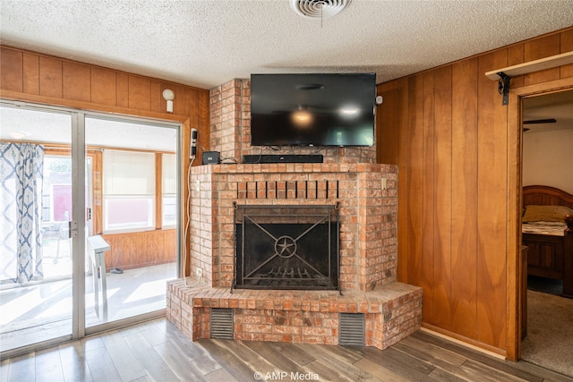 living room with dark wood-type flooring, wood walls, a fireplace, and a textured ceiling