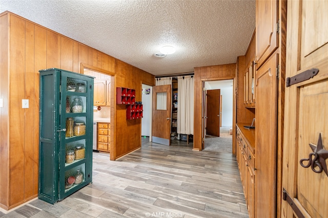 hall featuring light hardwood / wood-style floors, wooden walls, and a textured ceiling