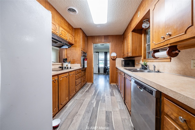 kitchen with wood walls, sink, a textured ceiling, light hardwood / wood-style flooring, and black appliances