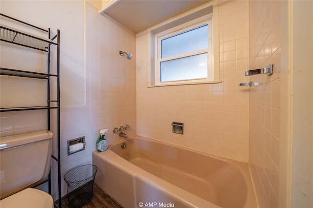 bathroom with wood-type flooring, tiled shower / bath, tile walls, and toilet