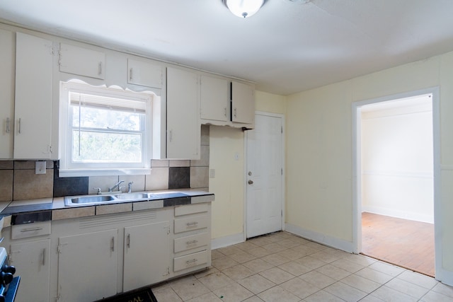 kitchen featuring decorative backsplash, white cabinetry, sink, and light tile patterned floors