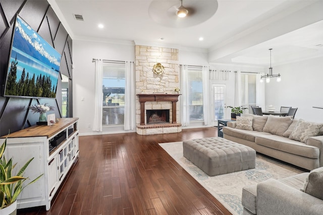 living room with dark wood-type flooring, crown molding, a stone fireplace, and a healthy amount of sunlight