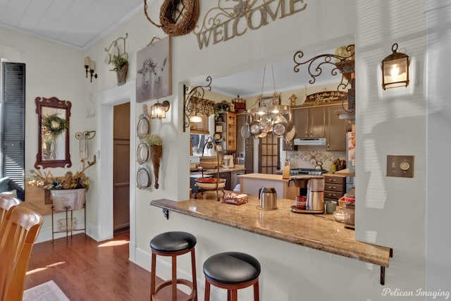 kitchen with a breakfast bar, light stone counters, dark hardwood / wood-style floors, kitchen peninsula, and crown molding