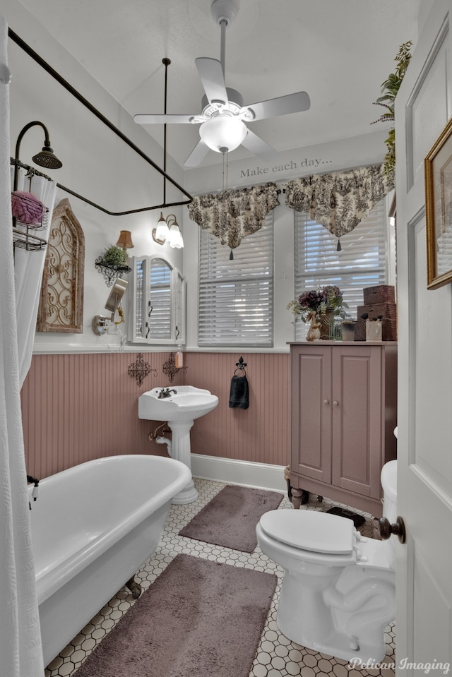 bathroom with ceiling fan with notable chandelier, tile patterned floors, a bathtub, and toilet