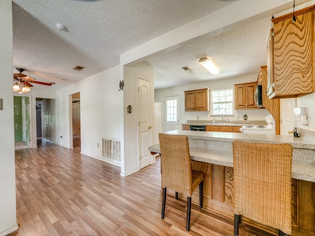 kitchen featuring light hardwood / wood-style floors, kitchen peninsula, white stove, a textured ceiling, and ceiling fan