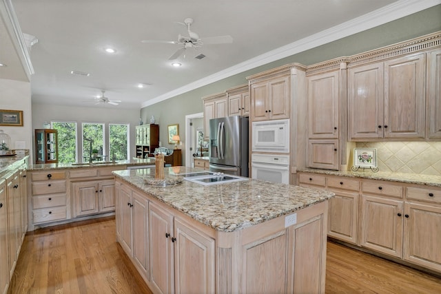 kitchen with a center island, light brown cabinets, tasteful backsplash, light hardwood / wood-style flooring, and white appliances