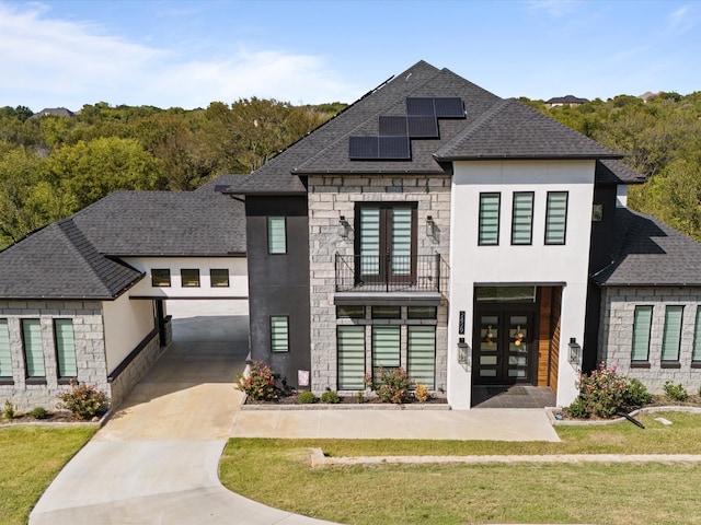 view of front of home with a balcony, solar panels, a front yard, and french doors