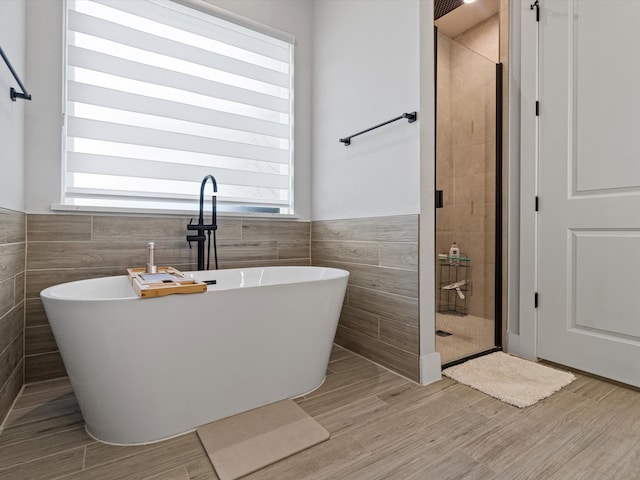 bathroom featuring independent shower and bath, hardwood / wood-style flooring, and tile walls