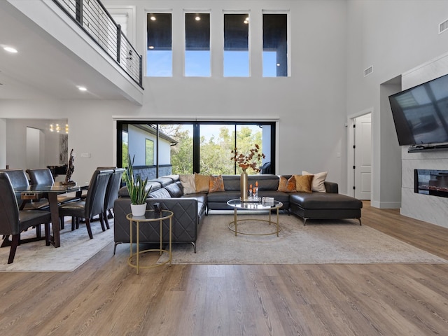 living room with light wood-type flooring, a towering ceiling, and a fireplace