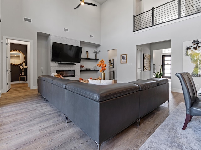 living room with light hardwood / wood-style floors, a high ceiling, a large fireplace, and ceiling fan