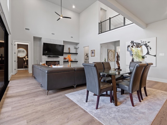 dining space with light wood-type flooring, a high ceiling, a fireplace, and ceiling fan