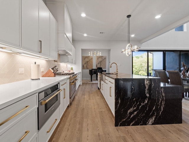 kitchen with pendant lighting, light hardwood / wood-style flooring, white cabinetry, appliances with stainless steel finishes, and a notable chandelier