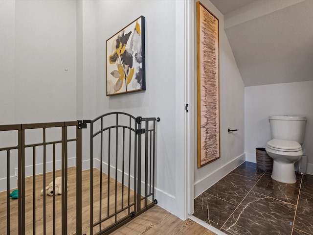 interior space featuring toilet, marble finish floor, baseboards, and vaulted ceiling