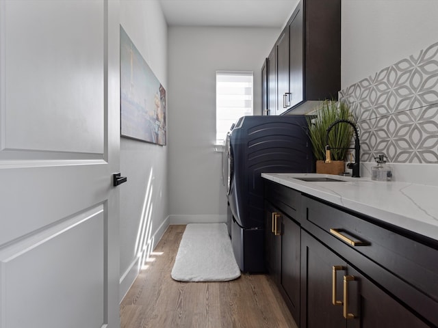 clothes washing area featuring cabinets, light hardwood / wood-style floors, sink, and washing machine and clothes dryer