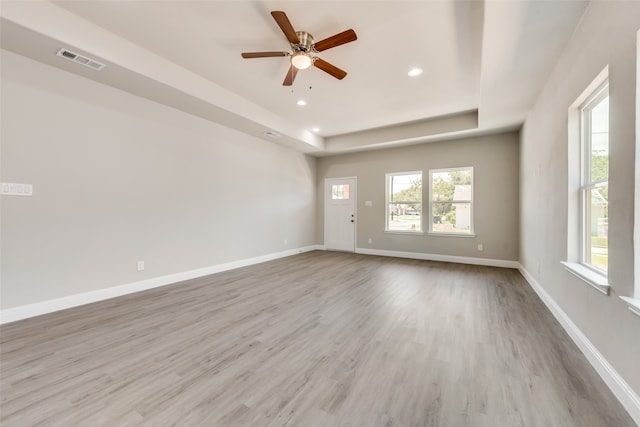 empty room with a tray ceiling, hardwood / wood-style floors, and ceiling fan