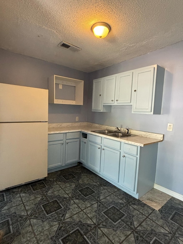 kitchen with a textured ceiling, white refrigerator, and sink