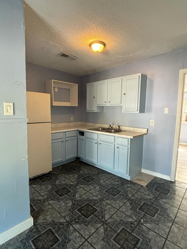 kitchen with white cabinets, sink, white fridge, and a textured ceiling