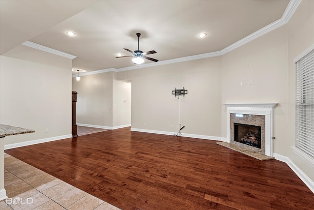 unfurnished living room featuring a premium fireplace, ceiling fan, ornamental molding, and hardwood / wood-style flooring