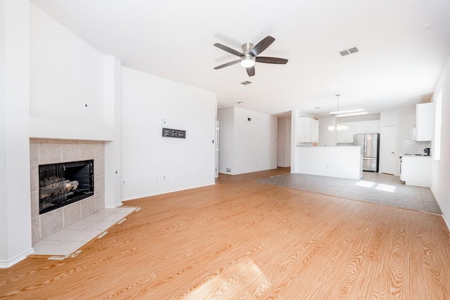 unfurnished living room featuring ceiling fan with notable chandelier, a fireplace, and light hardwood / wood-style flooring