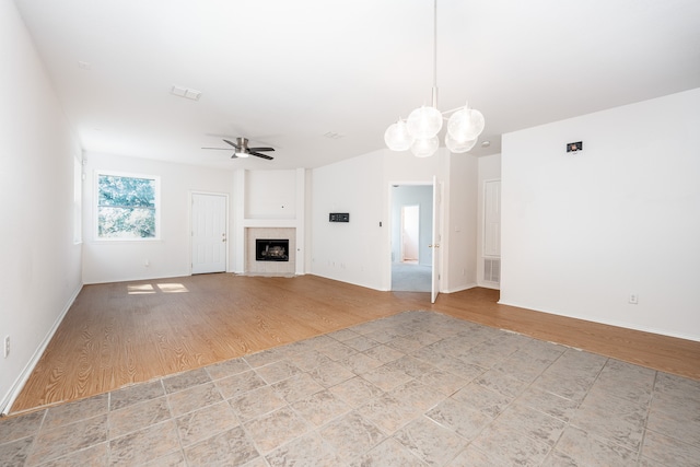 unfurnished living room with ceiling fan with notable chandelier, light hardwood / wood-style flooring, and a tiled fireplace