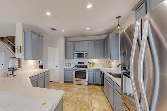 kitchen with gray cabinetry, backsplash, appliances with stainless steel finishes, and decorative light fixtures