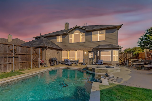 back house at dusk featuring a patio and a pool with hot tub