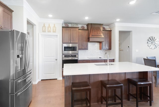 kitchen with a breakfast bar, sink, custom exhaust hood, a center island with sink, and appliances with stainless steel finishes