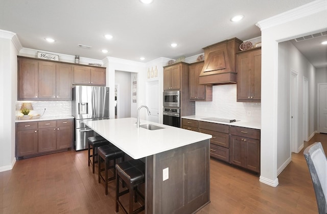 kitchen featuring a kitchen island with sink, stainless steel appliances, light countertops, premium range hood, and a sink