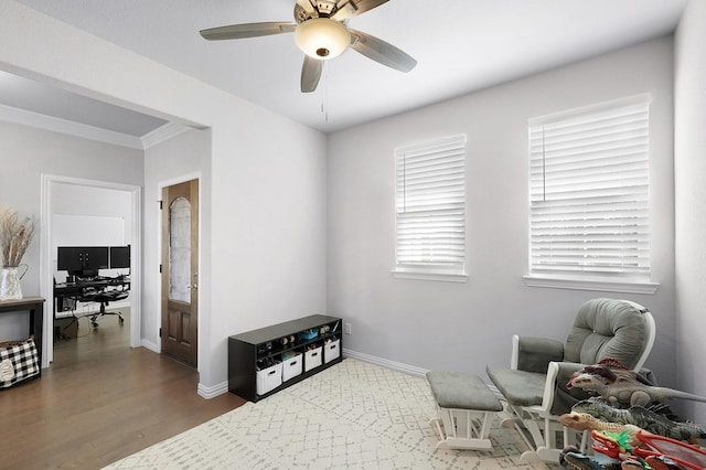 living area featuring crown molding, dark wood-type flooring, a ceiling fan, and baseboards