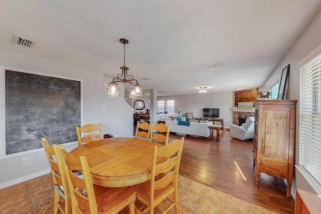 dining space featuring a brick fireplace, a textured ceiling, light tile patterned flooring, and plenty of natural light