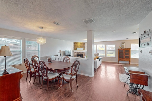 dining room featuring a textured ceiling, a brick fireplace, an inviting chandelier, and hardwood / wood-style flooring