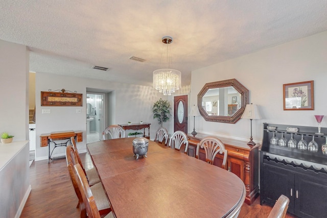 dining area with dark wood-type flooring, a textured ceiling, and a chandelier