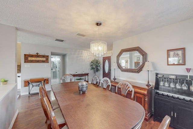 dining space featuring dark hardwood / wood-style flooring, a textured ceiling, and an inviting chandelier