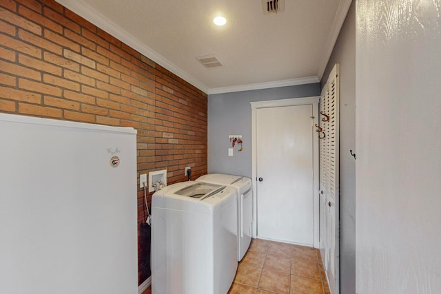 laundry area with brick wall, washer and dryer, crown molding, and light tile patterned floors