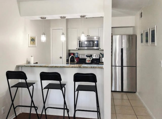 kitchen featuring appliances with stainless steel finishes, a kitchen breakfast bar, white cabinetry, decorative light fixtures, and dark stone counters