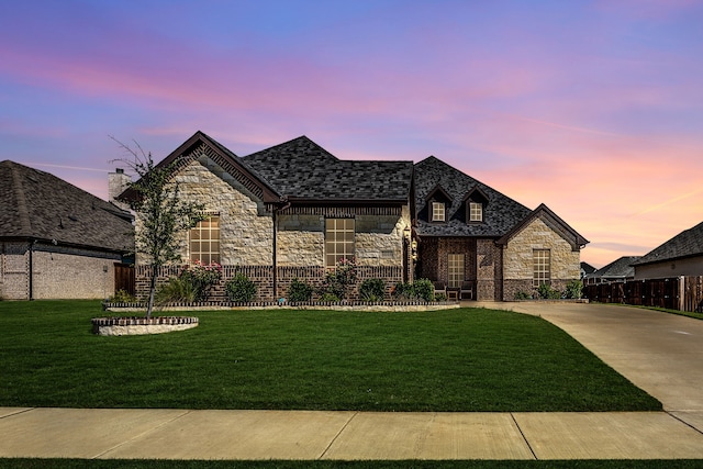 french country inspired facade with fence, a front yard, and stone siding