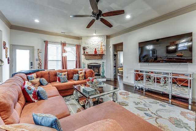 living room with crown molding, a stone fireplace, dark wood-type flooring, and ceiling fan