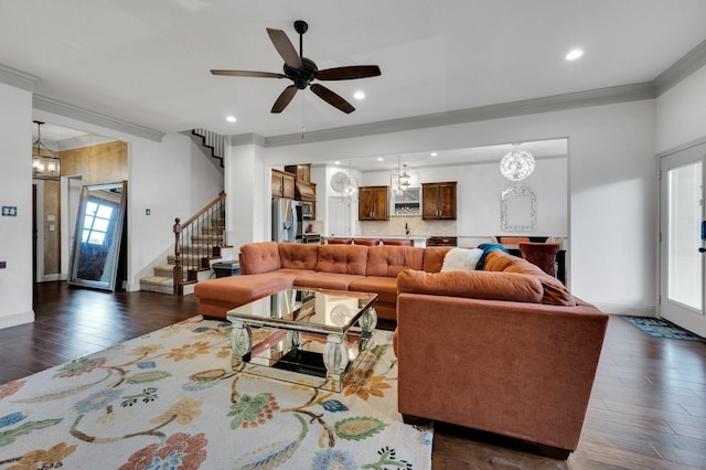 living room with stairway, baseboards, ornamental molding, dark wood-type flooring, and ceiling fan with notable chandelier