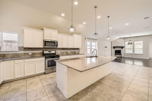 kitchen with lofted ceiling, a kitchen island with sink, light hardwood / wood-style flooring, appliances with stainless steel finishes, and decorative light fixtures