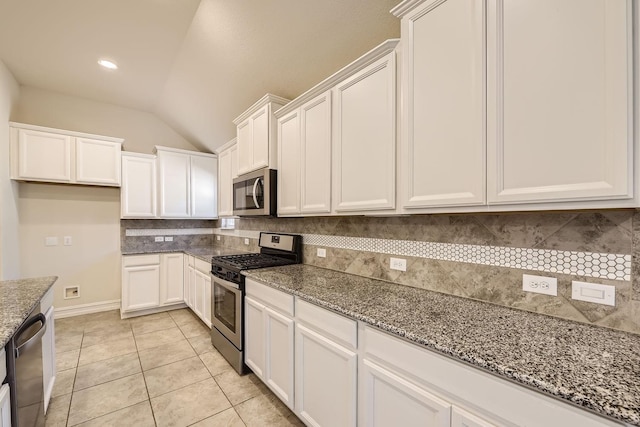 kitchen featuring vaulted ceiling, decorative backsplash, dark stone countertops, appliances with stainless steel finishes, and white cabinetry