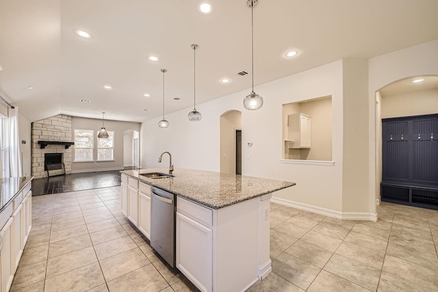 kitchen with light stone countertops, dishwasher, sink, a stone fireplace, and an island with sink