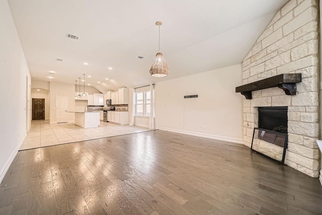 unfurnished living room with a stone fireplace, light hardwood / wood-style flooring, and lofted ceiling