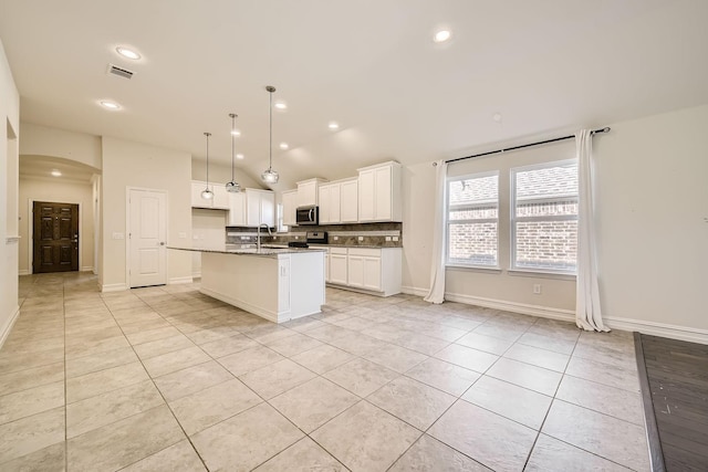 kitchen with white cabinets, light tile patterned floors, an island with sink, appliances with stainless steel finishes, and decorative light fixtures