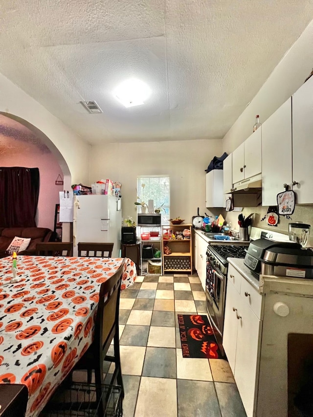 kitchen with white cabinetry, light tile patterned floors, stainless steel gas range, a textured ceiling, and white fridge with ice dispenser