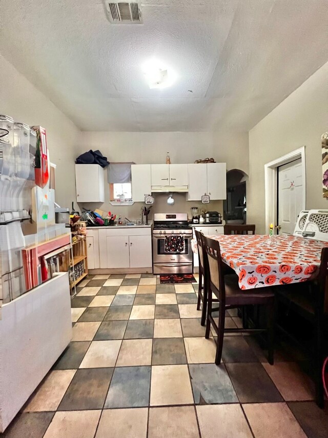 kitchen with a textured ceiling, stainless steel stove, and white cabinets