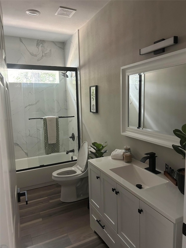 full bathroom featuring hardwood / wood-style floors, combined bath / shower with glass door, vanity, and toilet